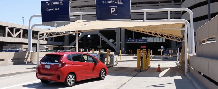 Red car driving up to the parking garage entry gate.