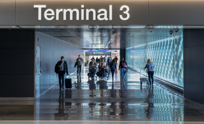 Terminal 3 sign with passengers and luggage walking down a corridor.