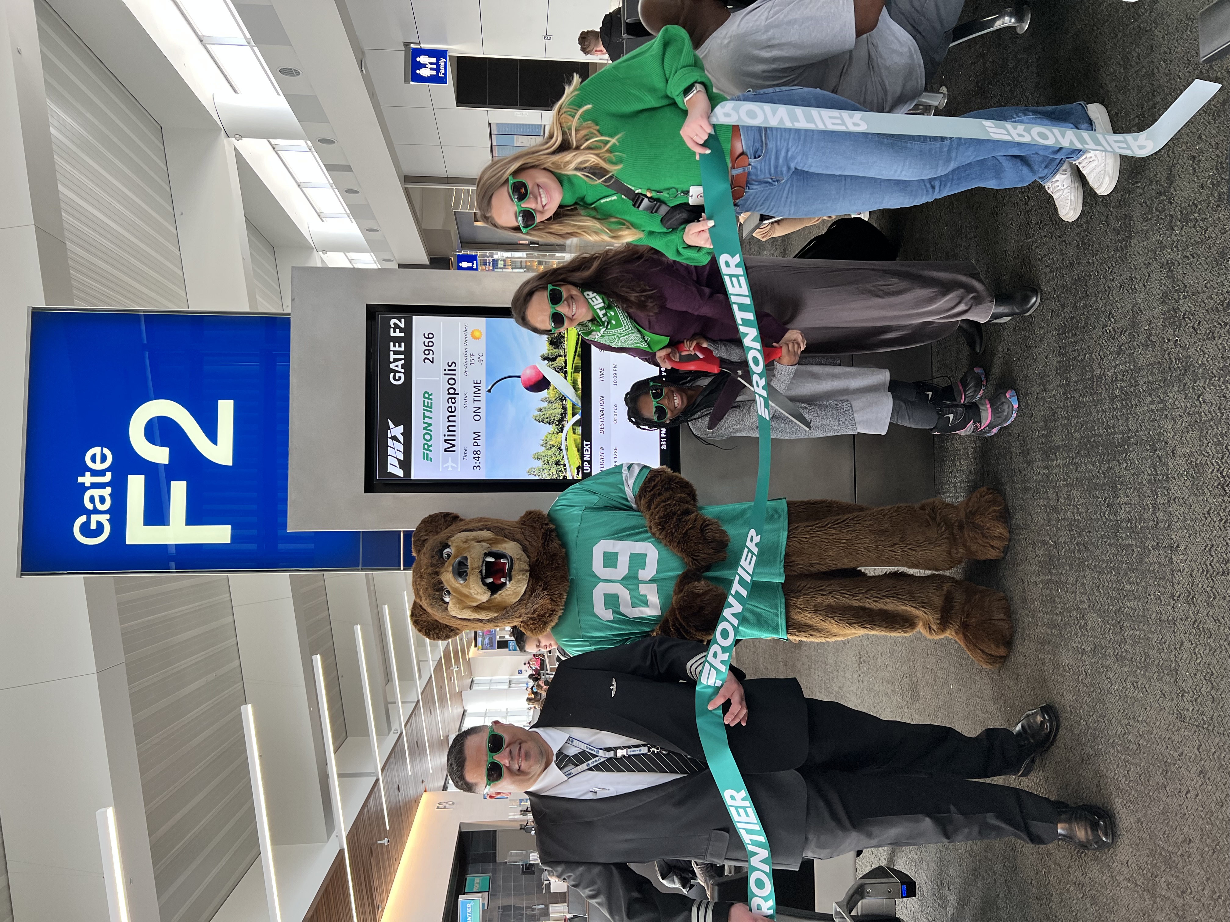 A person in bear costume and three people cutting a ribbon at Frontier Airlines